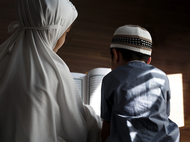 Vue arrière des enfants musulmans asiatiques religieux apprennent le Coran et étudient l'islam après avoir prié Dieu à la maison.