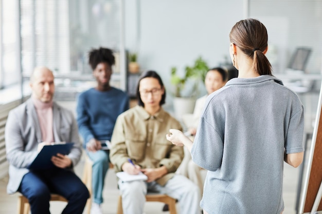 Vue arrière d'une entraîneure donnant une conférence ou un séminaire au bureau à divers groupes de personnes copiez l'espace