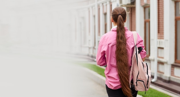 Vue arrière d'une étudiante en chemise rose avec sac à dos à l'extérieur