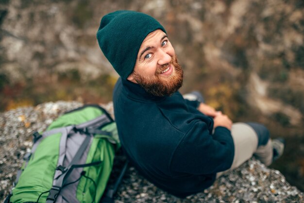 Vue arrière à l'extérieur portrait d'un randonneur heureux jeune homme au chapeau vert se sentir bien après une randonnée dans les montagnes Voyageur homme barbu souriant et se sentir heureux pendant le trekking dans son voyage