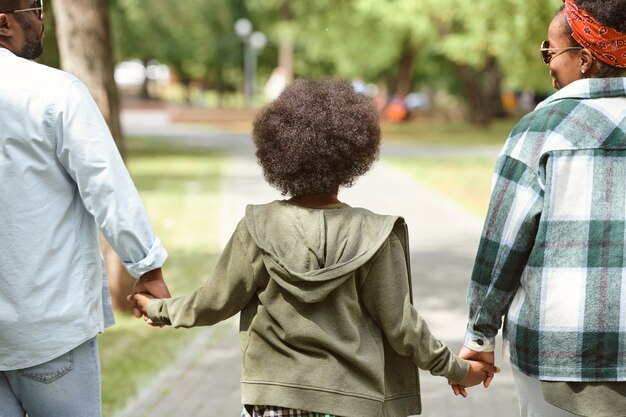 Vue arrière de la famille africaine contemporaine composée du père, de la mère et de leur fils se promenant dans le parc d'été