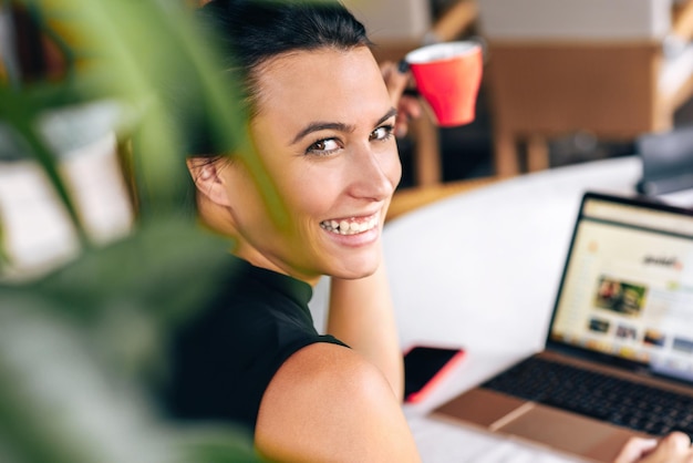 Vue arrière d'une femme d'affaires heureuse souriant et travaillant avec un ordinateur portable dans un café Portrait d'une jeune femme réussie lisant des nouvelles sur un ordinateur portable et buvant du café dans un restaurant le matin