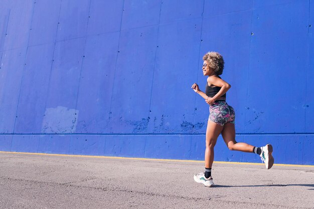 vue arrière d'une femme afro-américaine courant sur une piste urbaine avec fond bleu concept de sport et de style de vie actif, espace de copie pour le texte