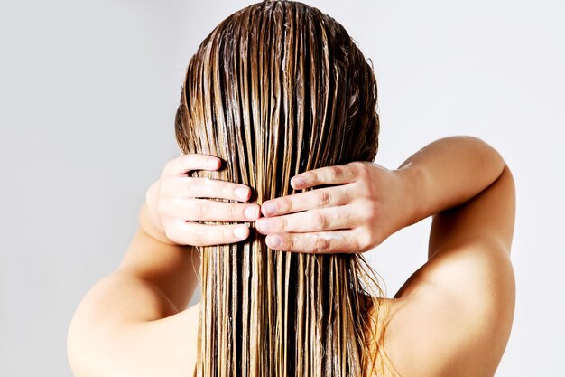 Photo vue arrière d'une femme appliquant du conditionneur sur les cheveux sur un fond blanc