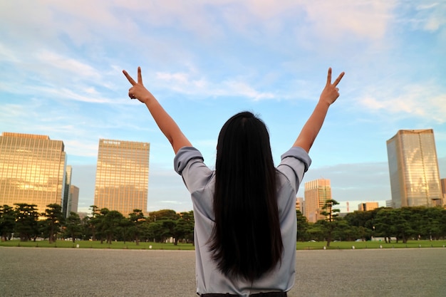 Vue arrière d&#39;une femme asiatique lève les mains avec un ciel bleu clair, nuages blancs et le bâtiment.