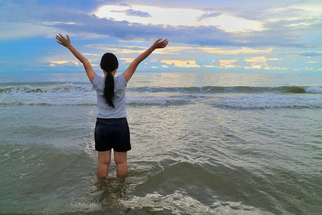 Vue arrière de la femme asiatique lèvent les mains avec la mer, le rythme des vagues, ciel coloré.