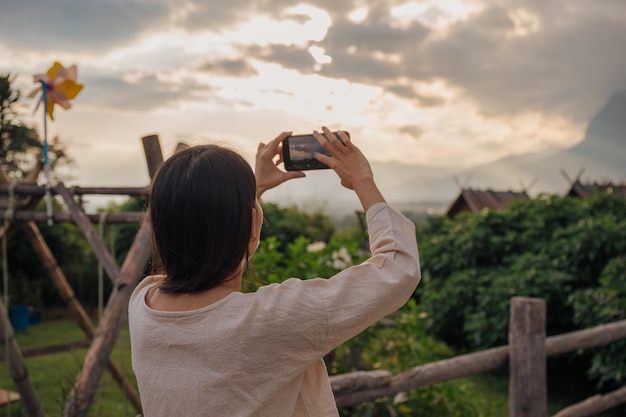 Vue arrière d'une femme asiatique prenant une vidéo de vue sur la montagne par smartphone sur un balcon en bois en vacances le soir