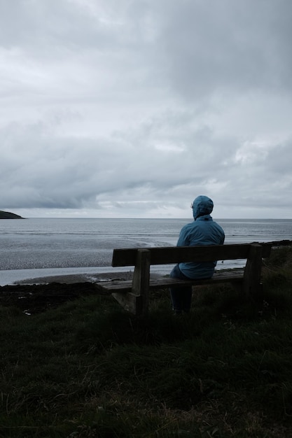 Vue arrière d'une femme assise sur un banc par la mer contre le ciel