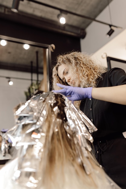 Photo vue arrière d'une femme assise dans un salon de beauté avec des cheveux enveloppés dans du papier d'aluminium, coiffeur coloriste regardant