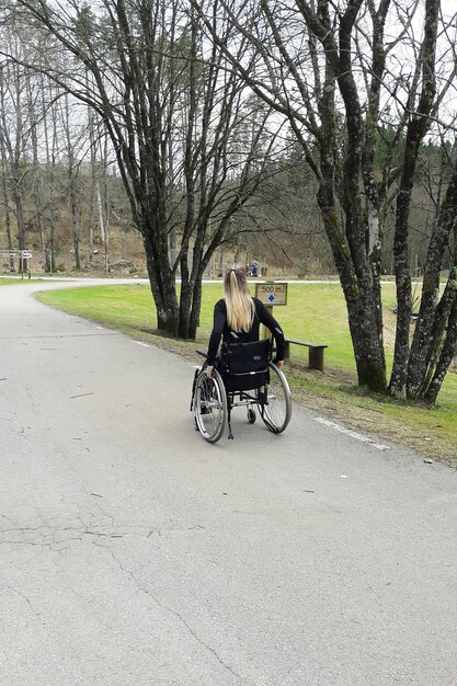 Photo vue arrière d'une femme assise sur un fauteuil roulant sur la route dans un parc