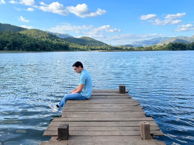 Vue arrière d'une femme assise sur une jetée au-dessus du lac contre le ciel