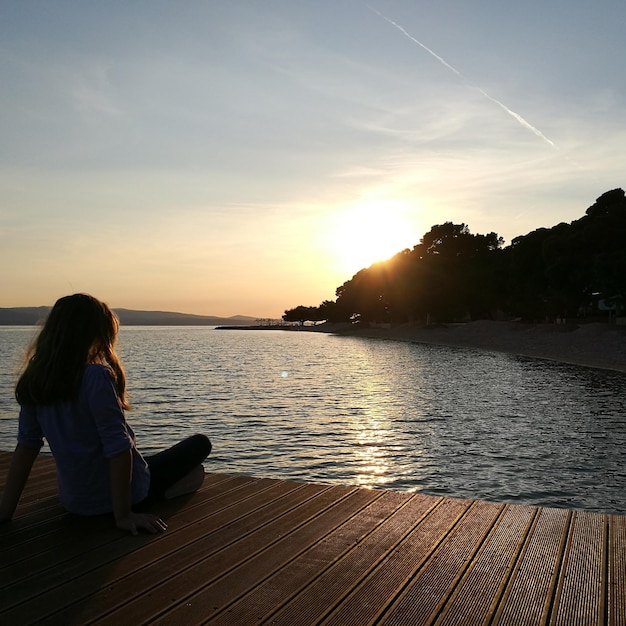 Photo vue arrière d'une femme assise sur une jetée au lac au coucher du soleil