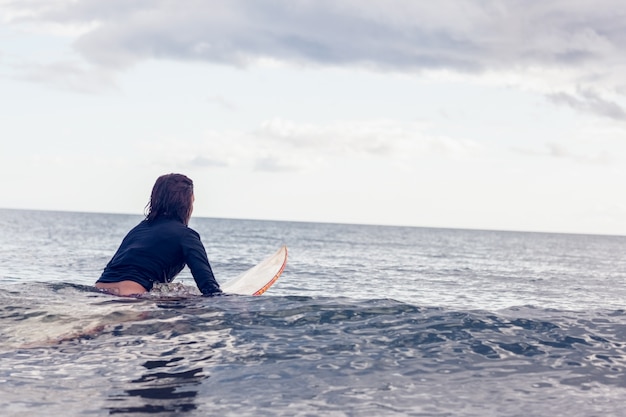 Vue arrière d&#39;une femme assise sur une planche de surf dans l&#39;eau