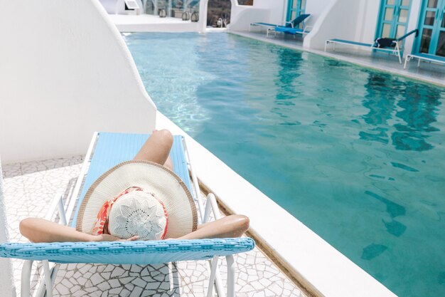 Vue arrière de la femme au chapeau d'été allongé sur une chaise de détente pour bronzer au bord de la piscine