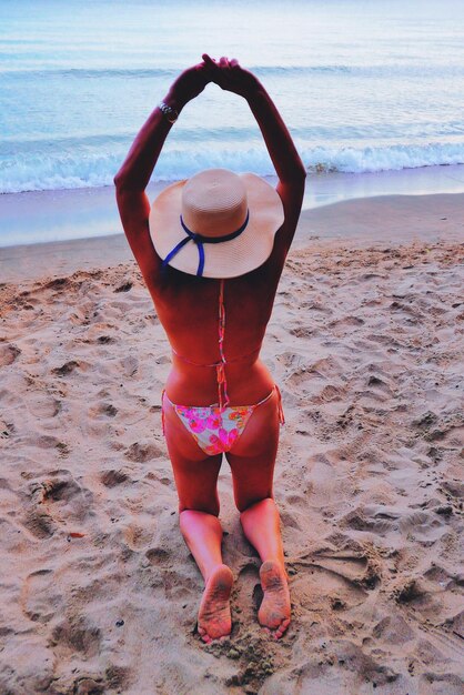 Photo vue arrière d'une femme aux bras levés agenouillée sur la plage