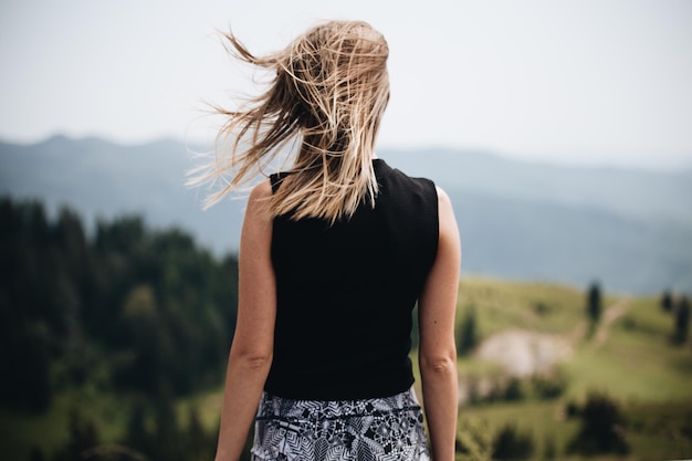 Vue arrière d'une femme aux cheveux blonds en désordre debout contre les montagnes
