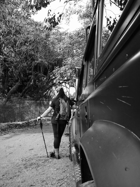 Photo vue arrière d'une femme avec un bâton de randonnée appuyé sur un véhicule