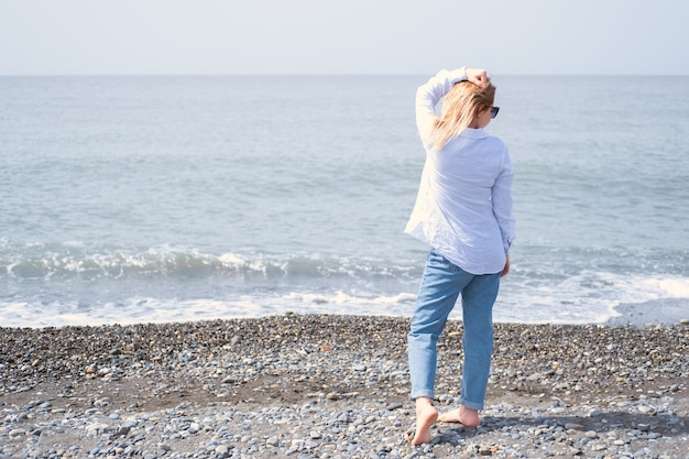 Vue arrière femme blonde debout sur le rivage de la mer aux beaux jours au printemps été