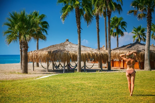 Vue arrière d'une femme blonde en maillot de bain marchant le long de la plage vers les bungalows