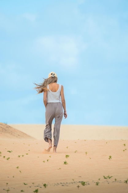Vue arrière d'une femme blonde marchant dans le désert de dunes par une journée ensoleillée