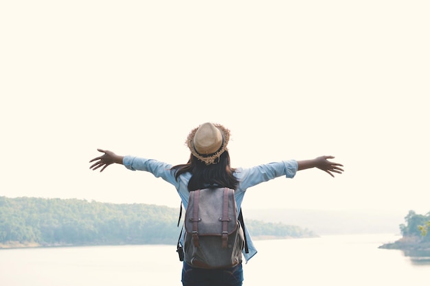 Photo vue arrière d'une femme avec les bras tendus debout près du lac contre un ciel clair