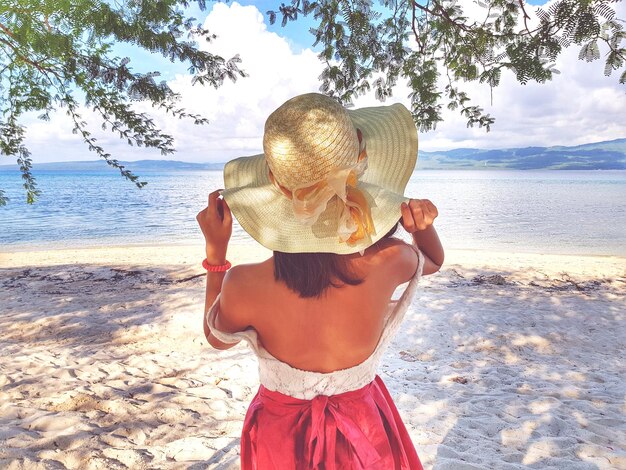 Photo vue arrière d'une femme en chapeau debout sur la plage contre le ciel