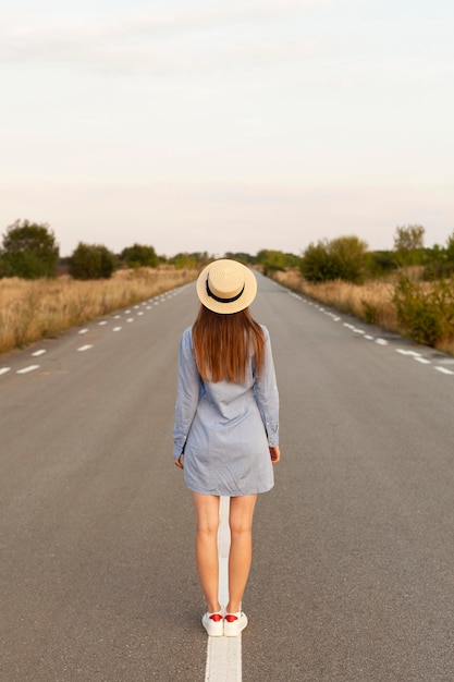 Vue arrière de la femme avec chapeau posant au milieu de la route