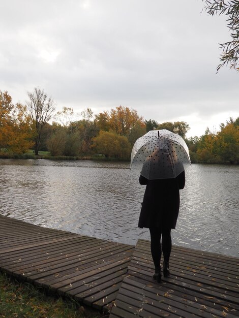 Photo vue arrière d'une femme debout au bord d'un lac contre le ciel