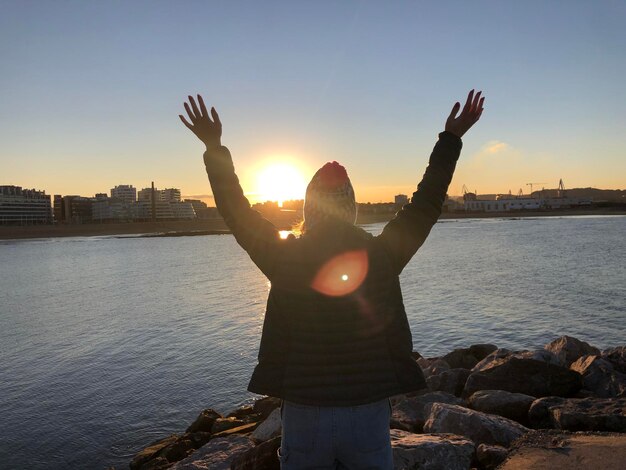 Photo vue arrière d'une femme debout au bord de la mer contre le ciel au coucher du soleil