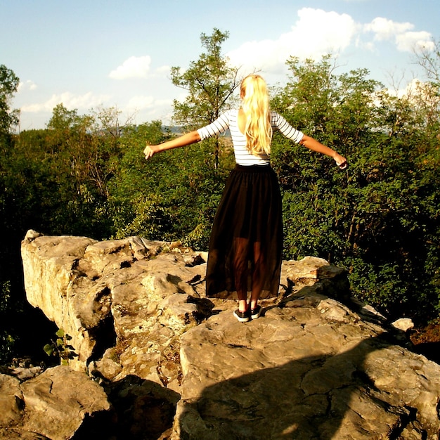 Photo vue arrière d'une femme debout avec les bras tendus sur une formation rocheuse