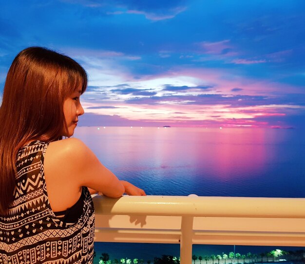 Vue arrière d'une femme debout contre la mer au coucher du soleil