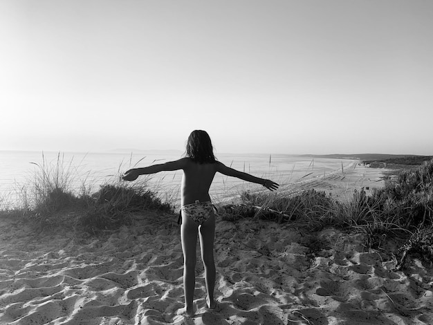 Vue arrière d'une femme debout sur la plage contre un ciel clair