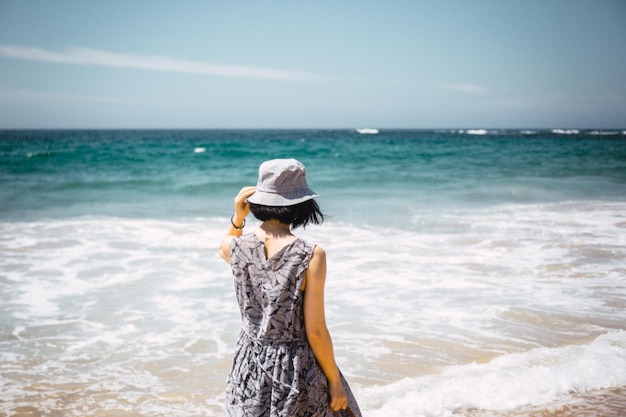 Vue arrière d'une femme debout sur la plage contre un ciel clair