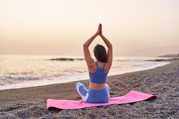 Vue arrière d'une femme de fitness calme et sereine satisfaite faisant du yoga, de la méditation et des exercices de respiration sur la plage au bord de la mer Soins de l'esprit mental et habitudes saines