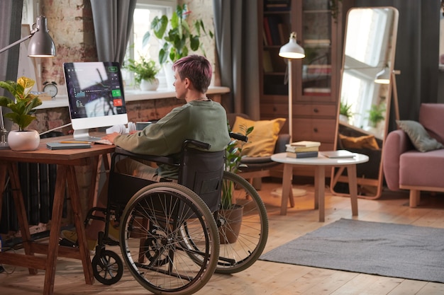 Vue arrière d'une femme handicapée travaillant comme programmeuse sur ordinateur avec un nouveau logiciel dans la chambre domestique