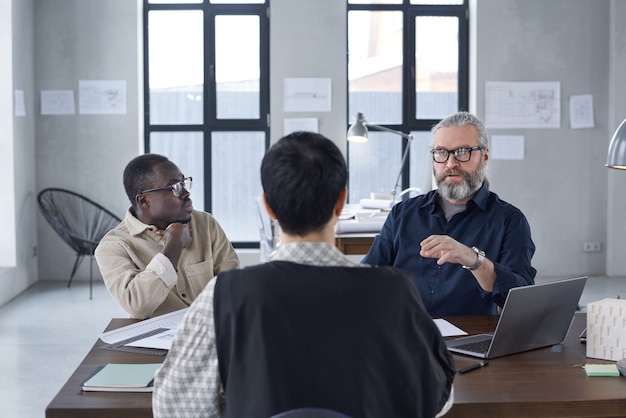 Vue arrière d'une femme leader assise à la table et parlant aux gens d'affaires lors d'une réunion au bureau