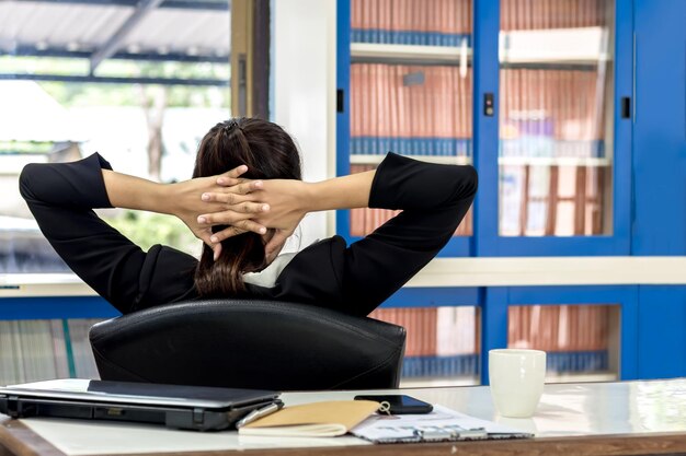 Vue arrière d'une femme avec les mains derrière la tête assise sur une chaise dans un bureau