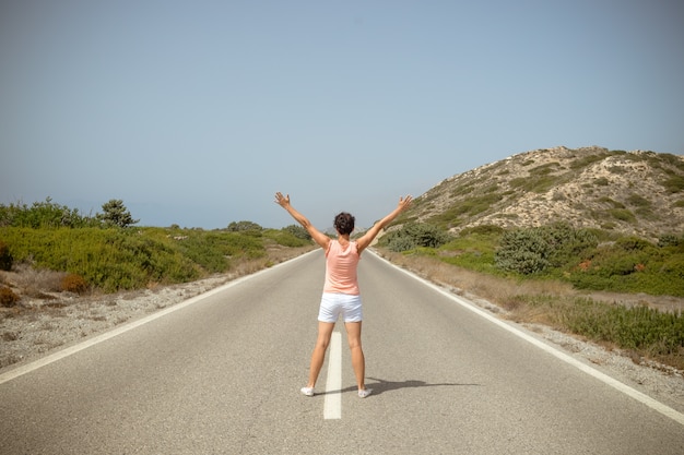 Vue arrière de la femme avec les mains levées debout sur une route goudronnée.