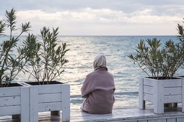 Photo vue arrière d'une femme en manteau à la recherche de la mer par temps froid.