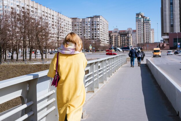 Vue arrière d'une femme marchant au milieu d'une rue vide portant un manteau jaune se promener dans la ville o...