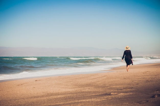 Photo vue arrière d'une femme marchant sur le rivage contre un ciel clair