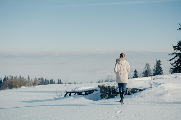 Vue arrière d'une femme marchant sur une terre couverte de neige contre le ciel pendant l'hiver