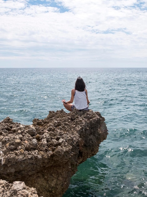 Photo vue arrière d'une femme méditant sur un rocher contre la mer