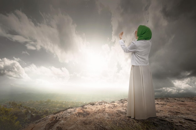 La vue arrière d'une femme musulmane dans un voile levant la main et priant