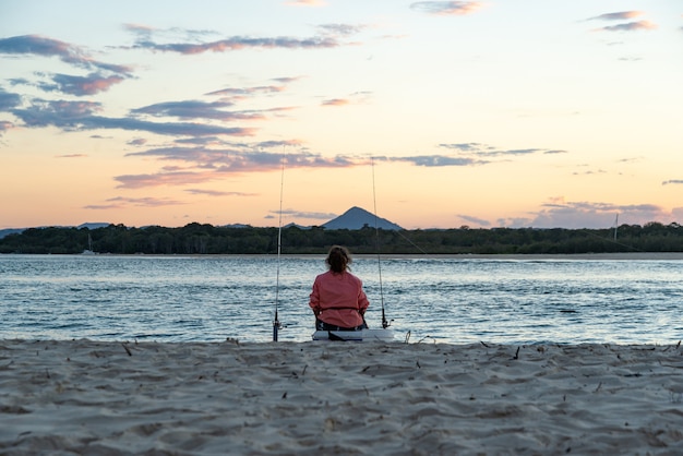 Vue arrière d'une femme pêchant sur la plage au coucher du soleil à Noosa, en Australie.