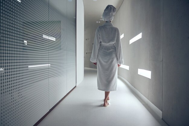 Vue arrière d'une femme en peignoir marchant le long du couloir dans un salon spa