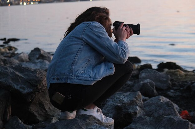 Photo vue arrière d'une femme photographiant sur un rocher à la plage