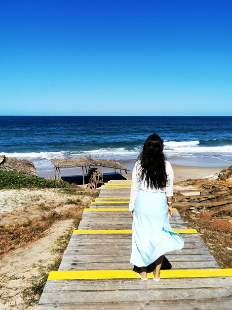 Photo vue arrière d'une femme sur la plage contre un ciel dégagé