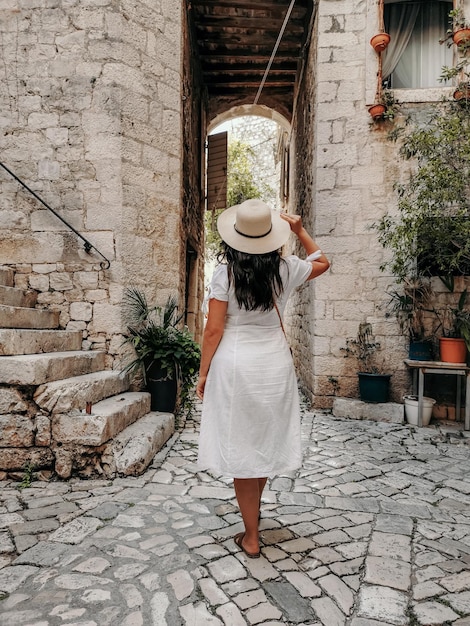 Vue arrière d'une femme portant une robe blanche marchant dans une vieille rue idyllique de la ville de Trogir, en Croatie.