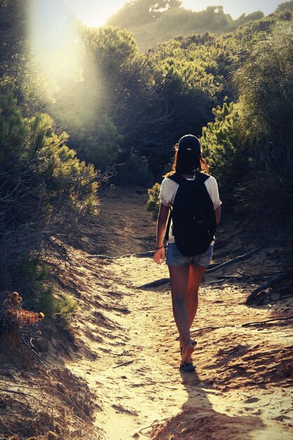 Photo vue arrière d'une femme randonneuse sur une route de terre dans la forêt